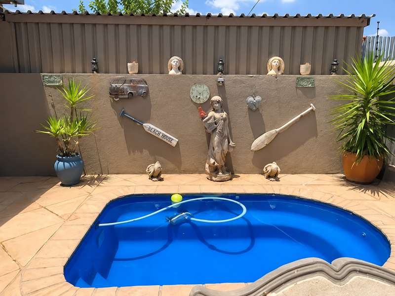 A compact swimming pool area featuring a paved surround and a decorative boundary wall with integrated lighting and landscaping.
