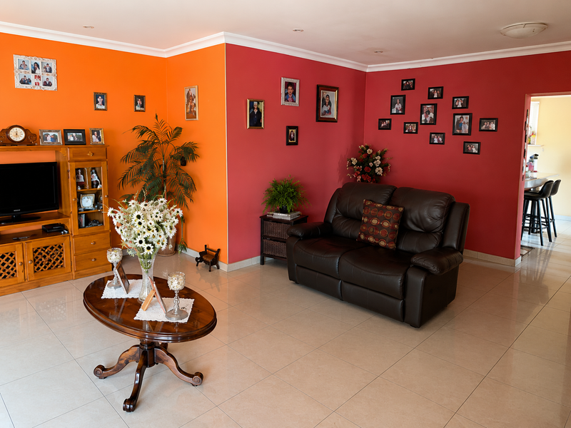 A spacious living room featuring tiled flooring and vibrant accent walls, offering a bright and open layout with a view into the adjacent kitchen area.