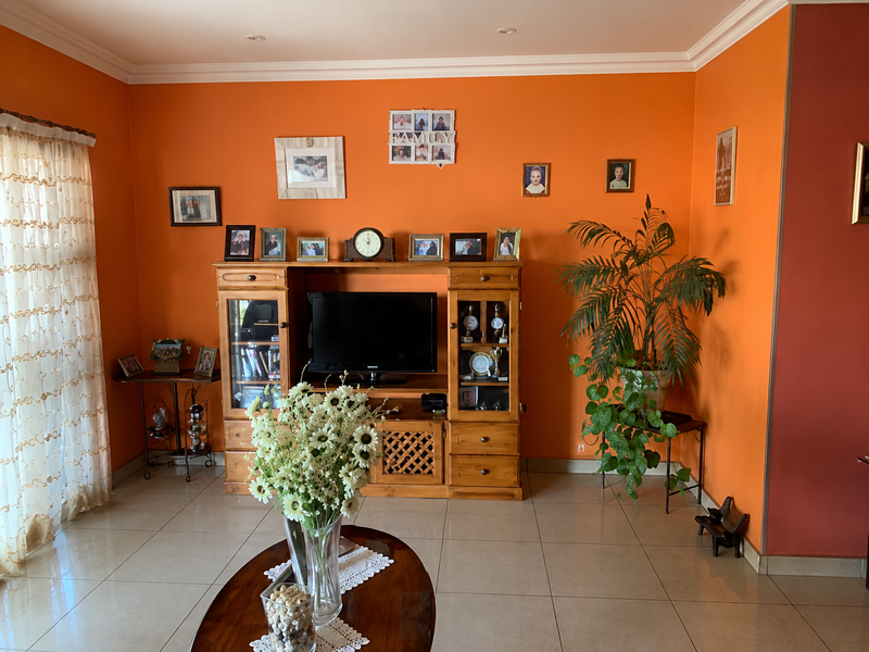A living room featuring tiled flooring, coved ceilings, and recessed lighting, currently finished with vibrant orange wall paint.