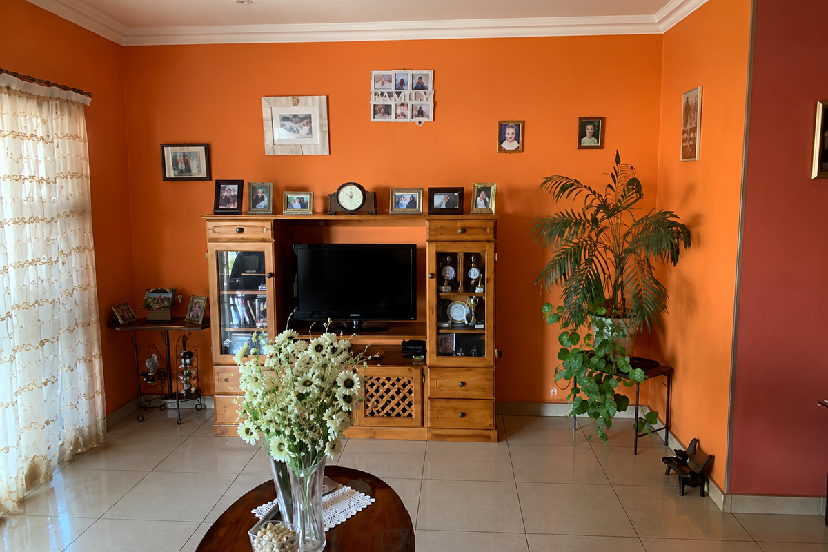 A living room featuring tiled flooring, coved ceilings, and recessed lighting, currently finished with vibrant orange wall paint.
