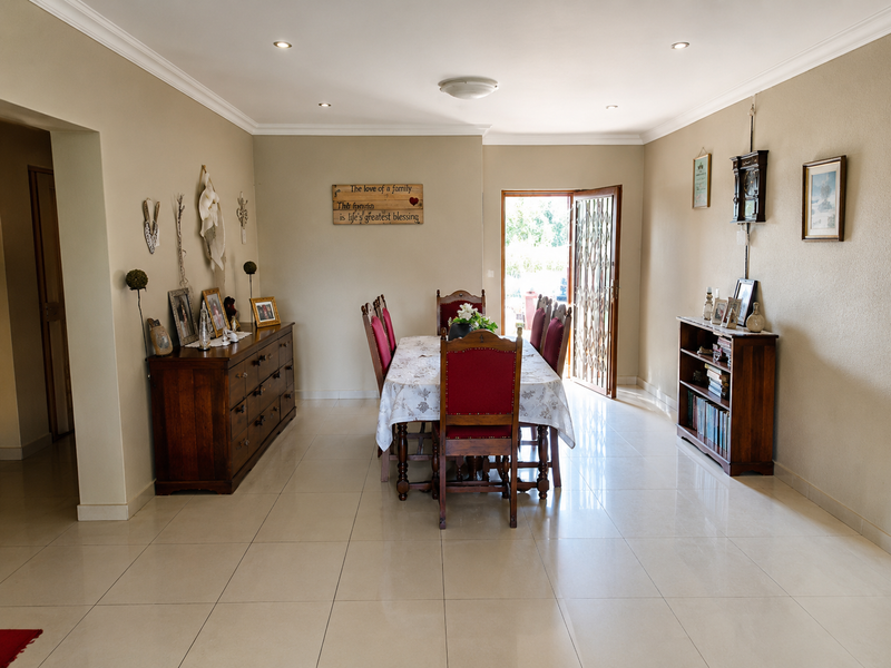A spacious dining room featuring neutral walls, polished ceramic floor tiles, and recessed lighting, with direct access to an outdoor area through a security gate.