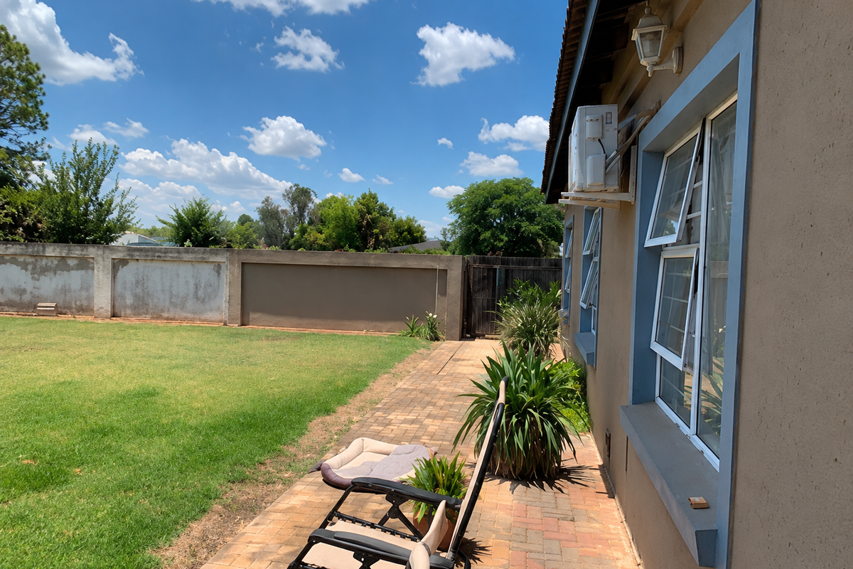 Rear exterior view featuring a paved patio area, lawn, perimeter wall, and wall-mounted air conditioning unit.