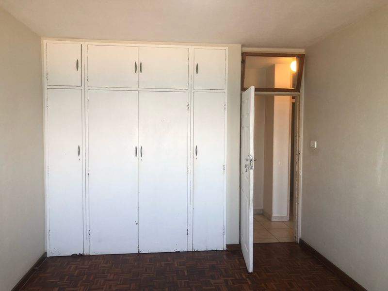 A bedroom featuring classic parquet flooring and extensive white built-in cupboards with overhead storage, leading into an adjacent hallway.