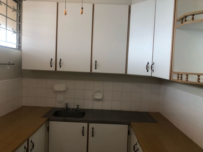 A functional kitchen space featuring laminate countertops, a stainless steel sink, tiled backsplash, and ample built-in cabinetry, ready for a modern update.