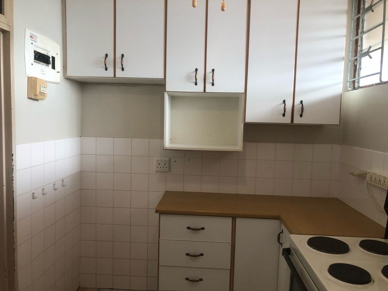 A functional kitchen area featuring white cabinetry, laminate countertops, tiled splashbacks, and a built-in electric stove.