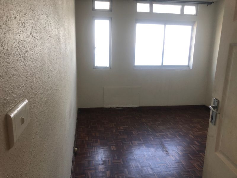 An empty bedroom featuring original parquet flooring and multiple windows, providing a blank canvas for renovation or staging.