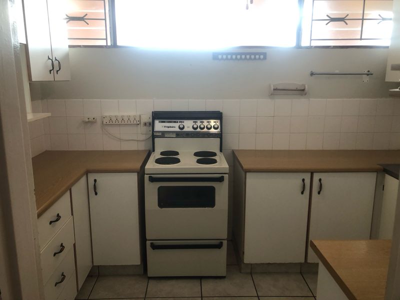A functional kitchen featuring built-in cabinetry, laminate countertops, a freestanding stove, and tiled finishes, offering potential for a modern renovation.