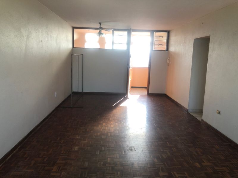 An empty living room featuring traditional parquet flooring, a ceiling fan, and direct access to an outdoor balcony area.