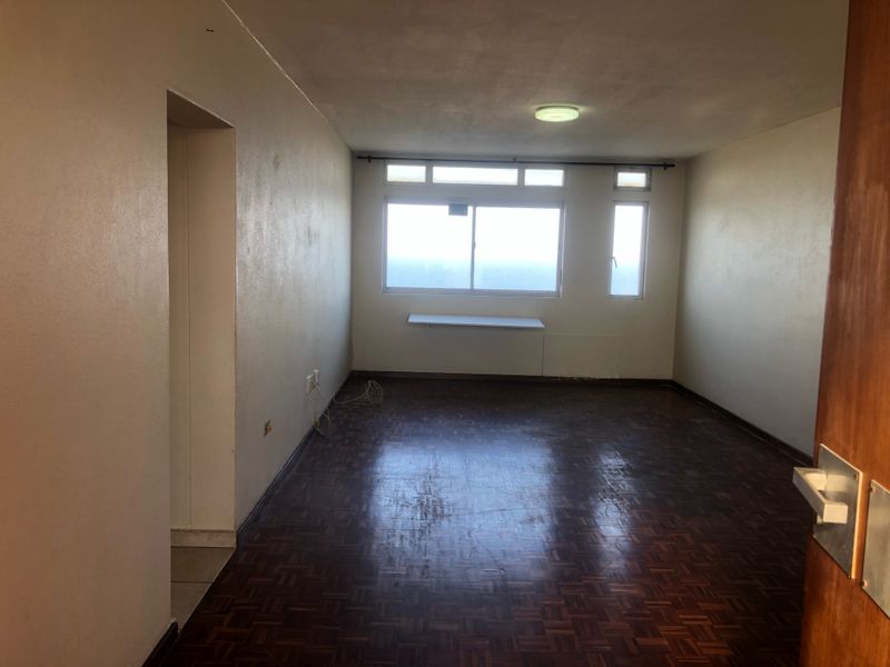 An empty living room featuring original parquet flooring, neutral walls, and a large window providing natural light.