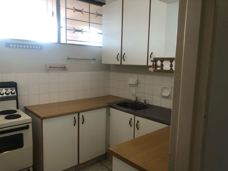 A compact kitchen featuring laminate countertops, white cabinetry, a stainless steel sink, and a tiled backsplash, requiring modernization to improve functionality and aesthetic appeal.
