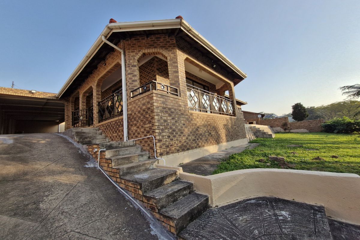 Rear view of a face brick house featuring a covered patio, concrete stairs, and a paved driveway leading to a garage area.