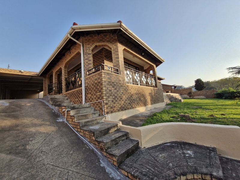 Rear view of a face brick house featuring a covered patio, concrete stairs, and a paved driveway leading to a garage area.