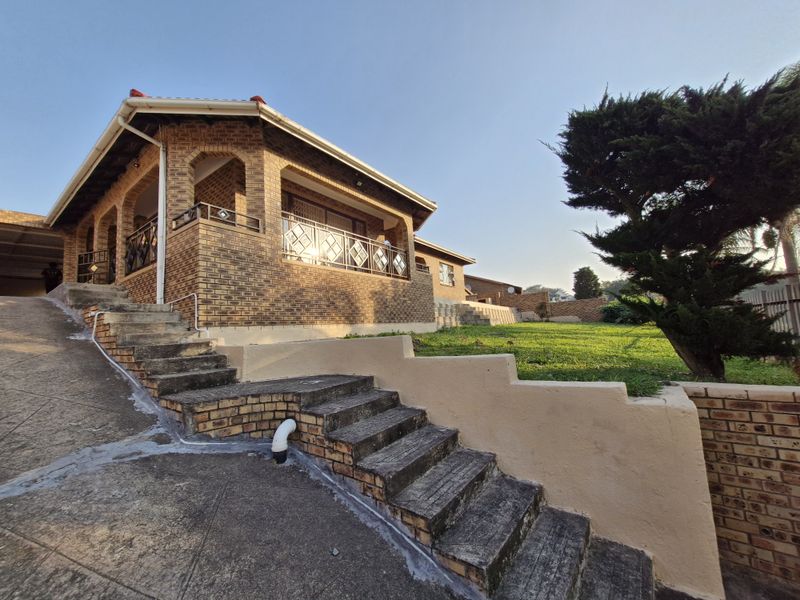 Front exterior view of a face brick house featuring a covered patio, concrete staircase, and a landscaped garden area.