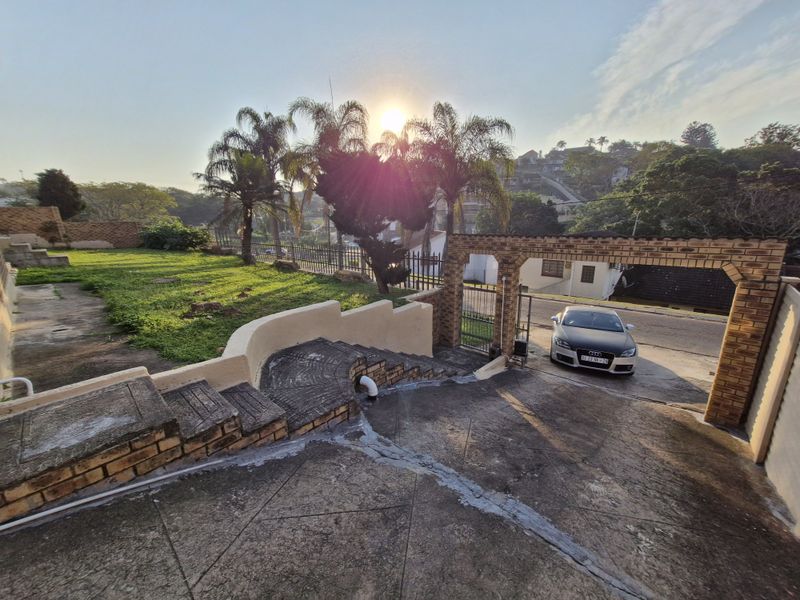 Front exterior view featuring a concrete driveway, brick boundary wall, gated entrance, and a sloped garden area.