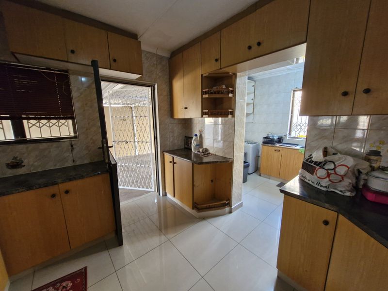 A functional kitchen featuring laminate cabinetry, tiled flooring, and direct access to an outdoor area secured with a metal gate.
