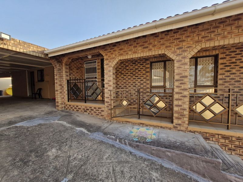 Front exterior view of a face brick house featuring a covered patio, metal security gates, and an adjacent carport area.