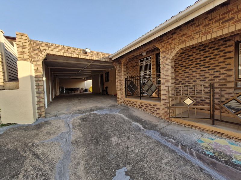 Front exterior view featuring a face brick facade, a covered carport area, and a concrete driveway with visible surface wear.