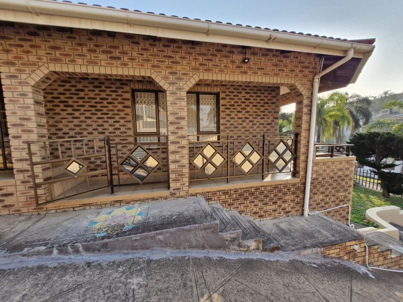 A covered patio area featuring face brick walls, decorative metal railings, and concrete access ramp and stairs leading to the entrance.