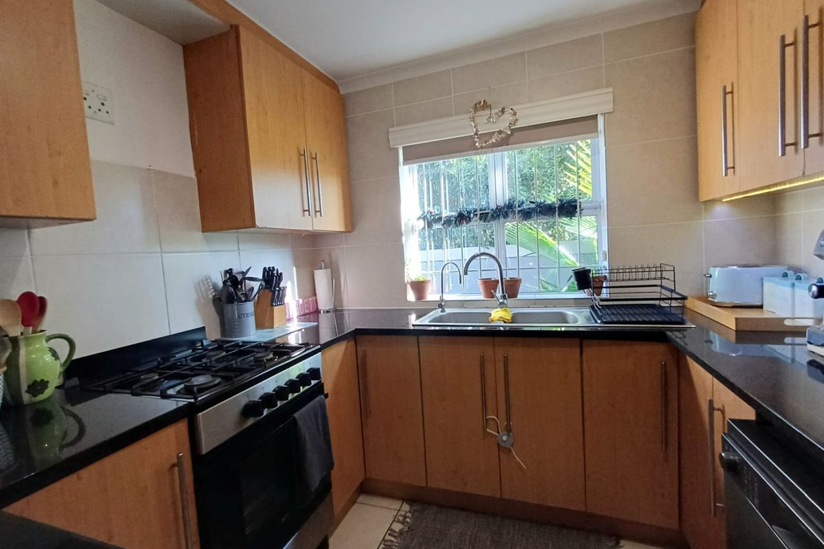 A functional kitchen featuring wood-finish cabinetry, granite countertops, a gas hob, and a tiled backsplash with a window overlooking the exterior.
