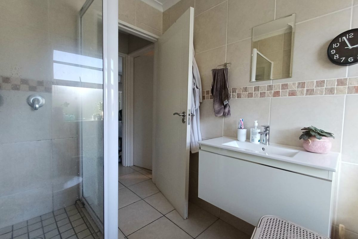 A functional bathroom featuring a glass shower enclosure, wall-mounted vanity with basin, and neutral tiled finishes throughout.