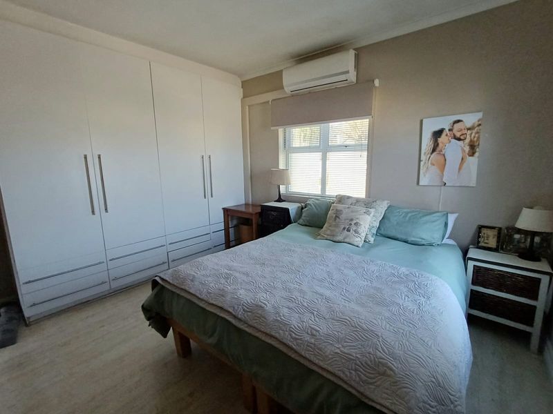 A well-maintained bedroom featuring extensive built-in cupboards, laminate flooring, and a wall-mounted split-system air conditioner for climate control.