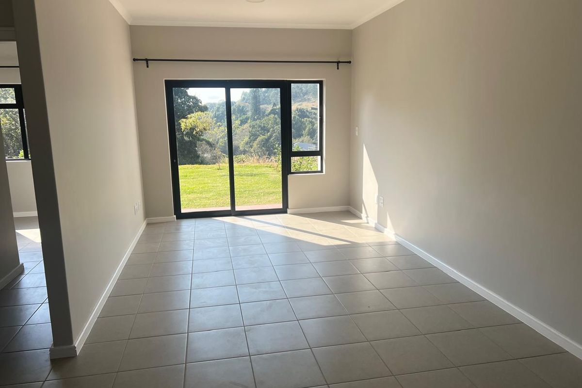 A bright, empty living room featuring neutral tiled flooring and a large sliding glass door that provides access to the outdoor area.