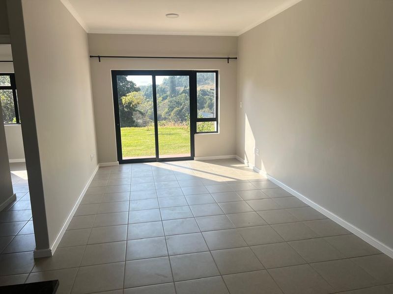 A bright, empty living room featuring neutral tiled flooring and a large sliding glass door that provides access to the outdoor area.