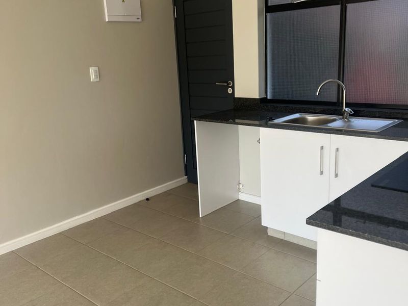 A clean, modern kitchen area featuring white cabinetry, dark granite countertops, a stainless steel sink, and neutral tiled flooring.