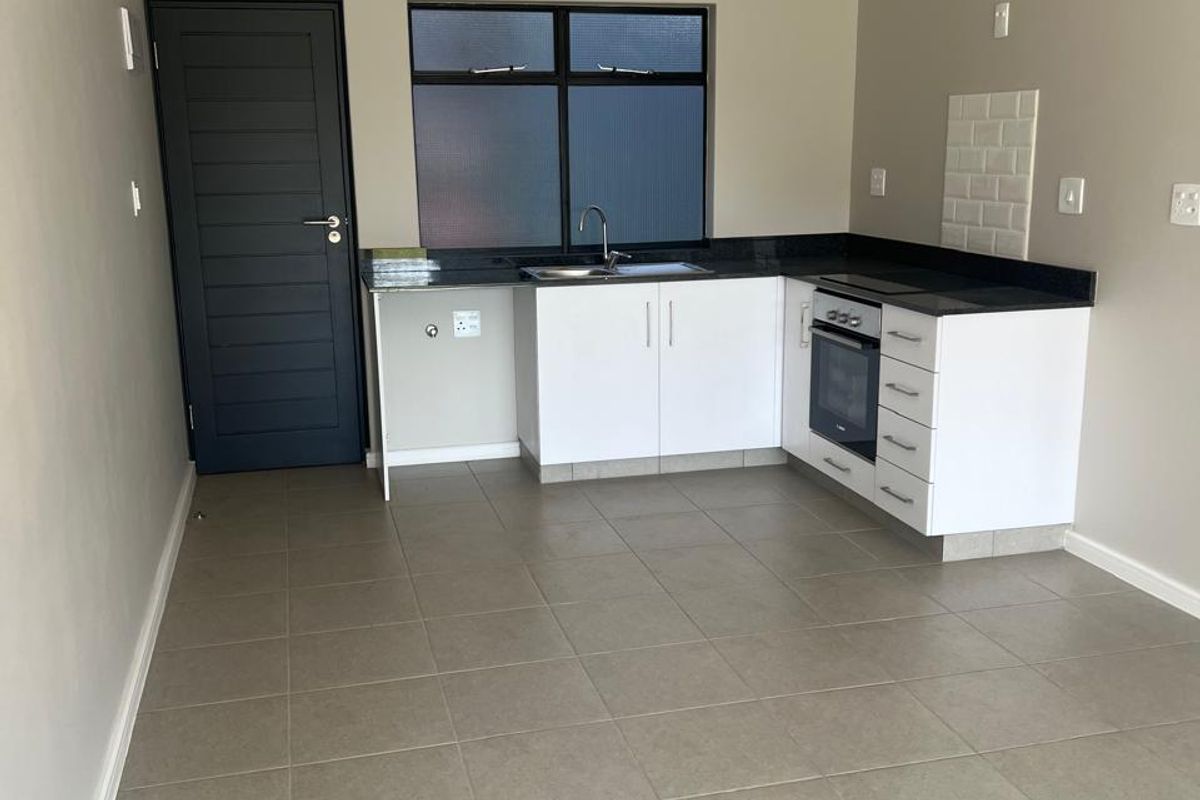 A clean, modern kitchen featuring white cabinetry, granite countertops, built-in oven, hob, and neutral tiled flooring in an open-plan layout.