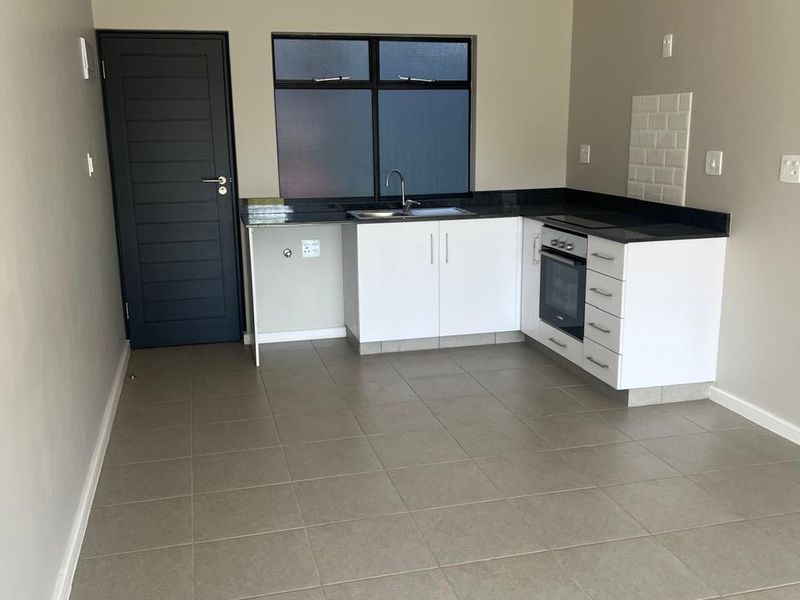 A clean, modern kitchen featuring white cabinetry, granite countertops, built-in oven, hob, and neutral tiled flooring in an open-plan layout.