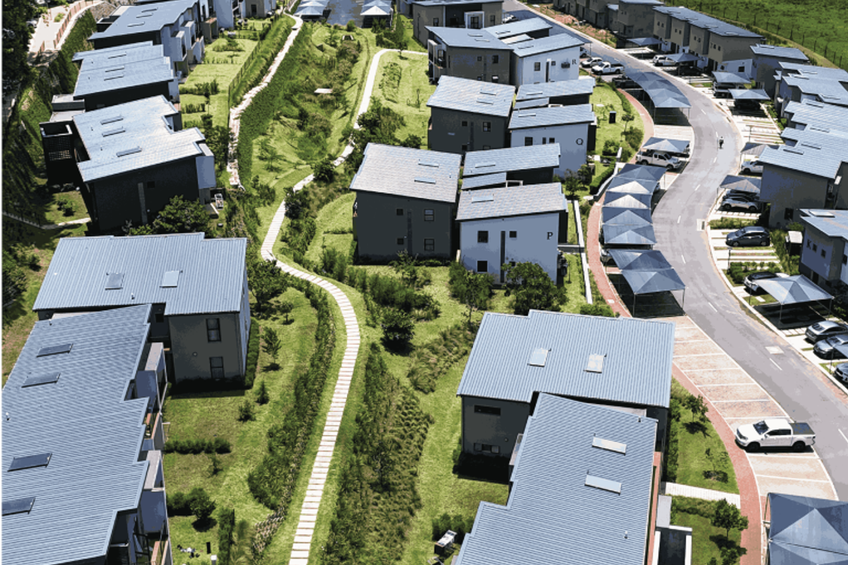 Aerial view of a modern residential apartment complex featuring contemporary architecture, metal roofs, landscaped green spaces, and dedicated carport parking areas.