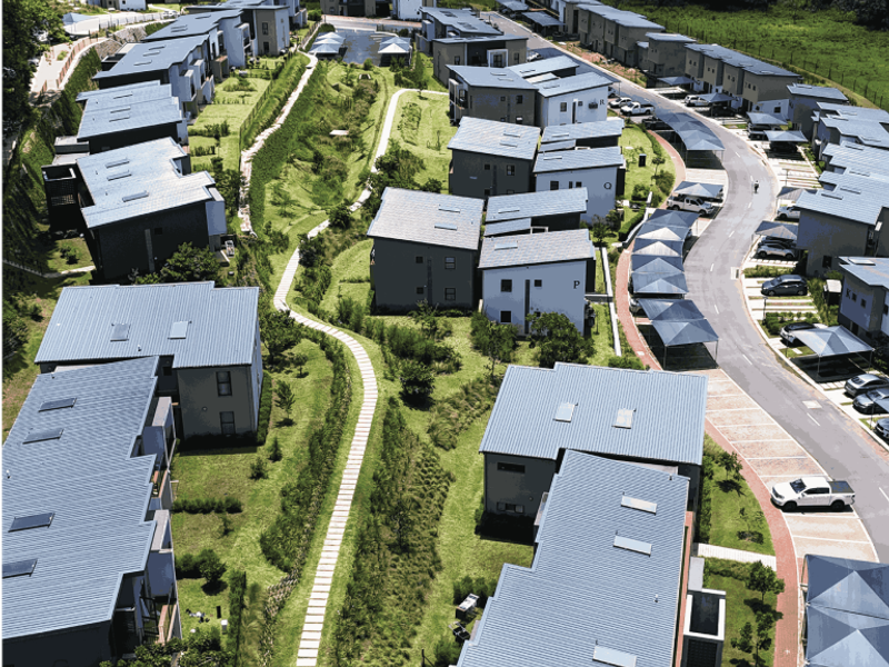 Aerial view of a modern residential apartment complex featuring contemporary architecture, metal roofs, landscaped green spaces, and dedicated carport parking areas.