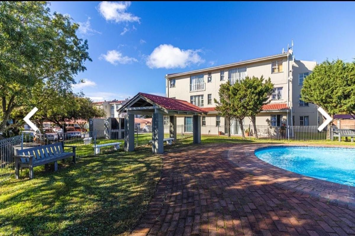 Communal pool area featuring a brick-paved deck, covered gazebo with built-in braai facilities, and landscaped garden surroundings within the apartment complex.