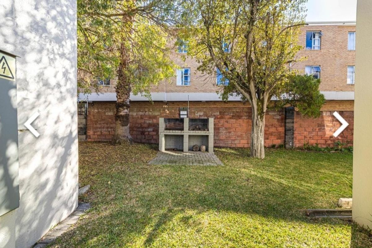 A rear garden area featuring a built-in brick braai, established trees, and a brick boundary wall with integrated electric fencing.