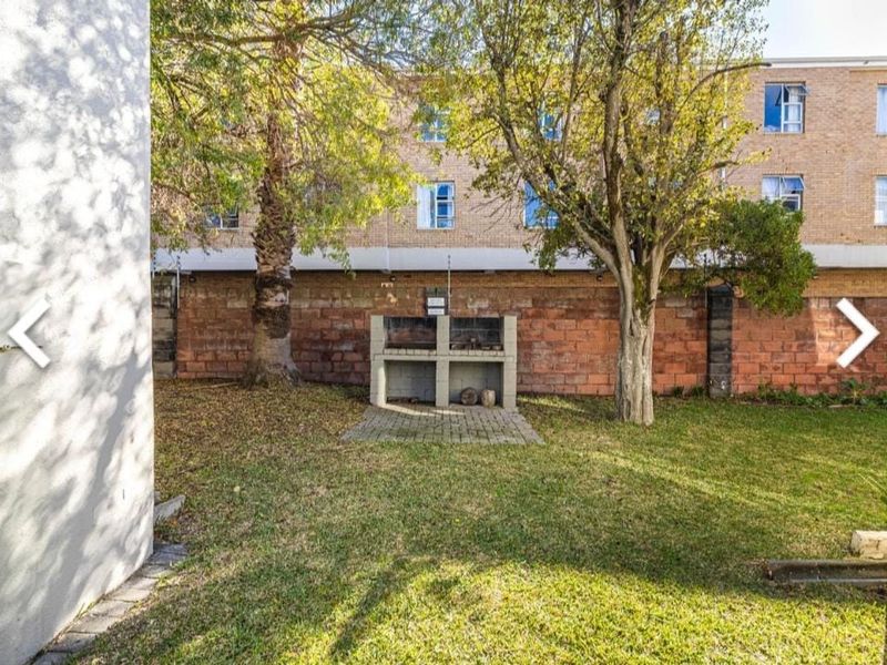 A rear garden area featuring a built-in brick braai, established trees, and a brick boundary wall with integrated electric fencing.