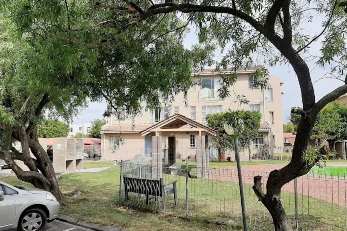 Rear view of the apartment complex featuring a communal garden, paved pathways, a covered gazebo, and built-in brick braai facilities.