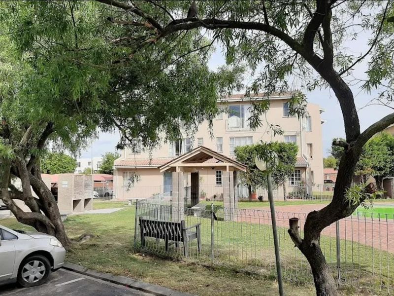 Rear view of the apartment complex featuring a communal garden, paved pathways, a covered gazebo, and built-in brick braai facilities.