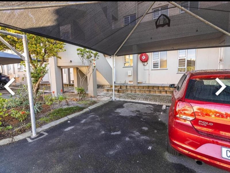 Exterior view of the apartment complex featuring a covered carport, paved driveway, and communal garden area with concrete access stairs.