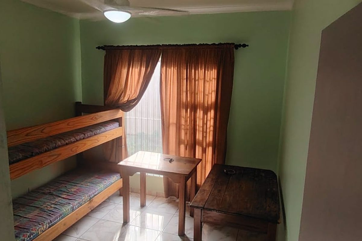 A bedroom featuring tiled flooring, a ceiling fan, and security bars on the window, providing a functional space with potential for cosmetic updates.