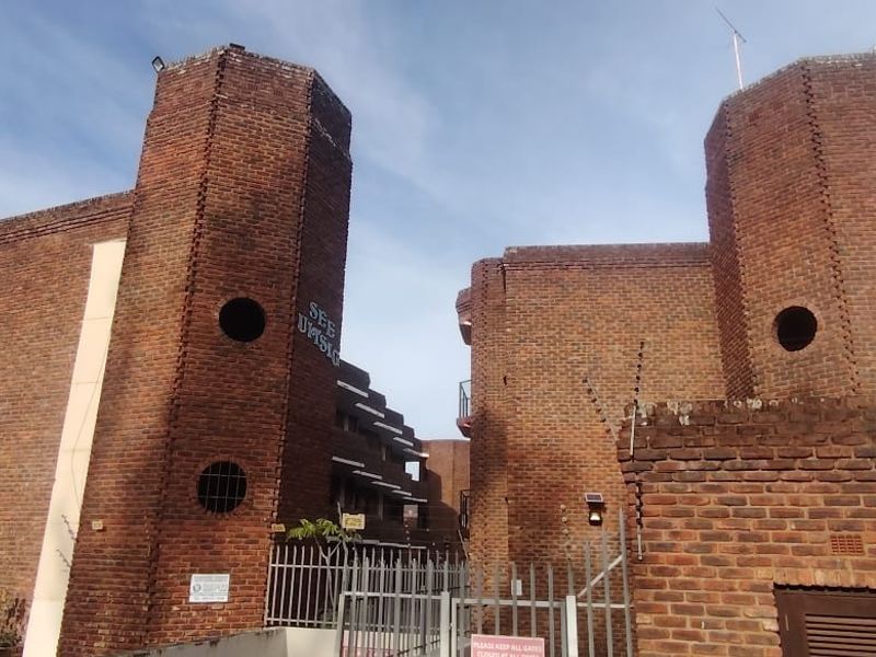 Front elevation of a townhouse complex featuring distinctive exposed brick towers, secure perimeter fencing, and gated access.