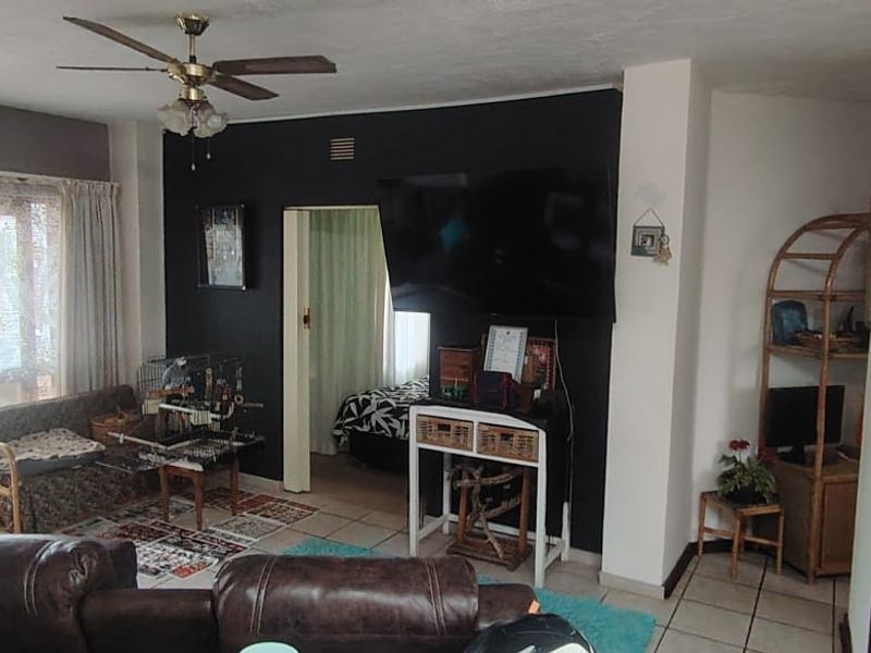 A living room area featuring tiled flooring, a ceiling fan, and access to an adjacent room.