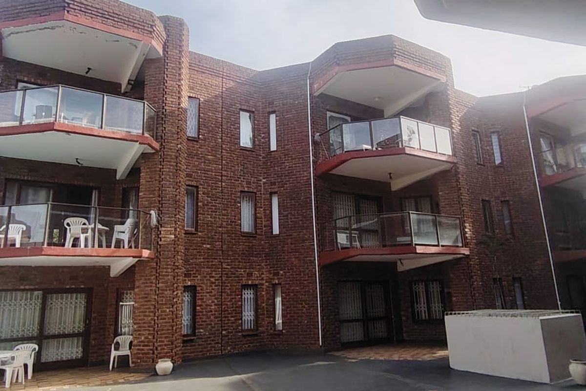 Rear view of a multi-story townhouse complex featuring exposed brick architecture, private balconies with glass balustrades, and a paved ground-level courtyard area.