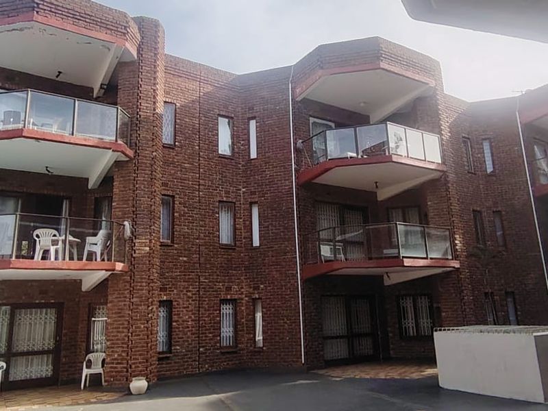 Rear view of a multi-story townhouse complex featuring exposed brick architecture, private balconies with glass balustrades, and a paved ground-level courtyard area.