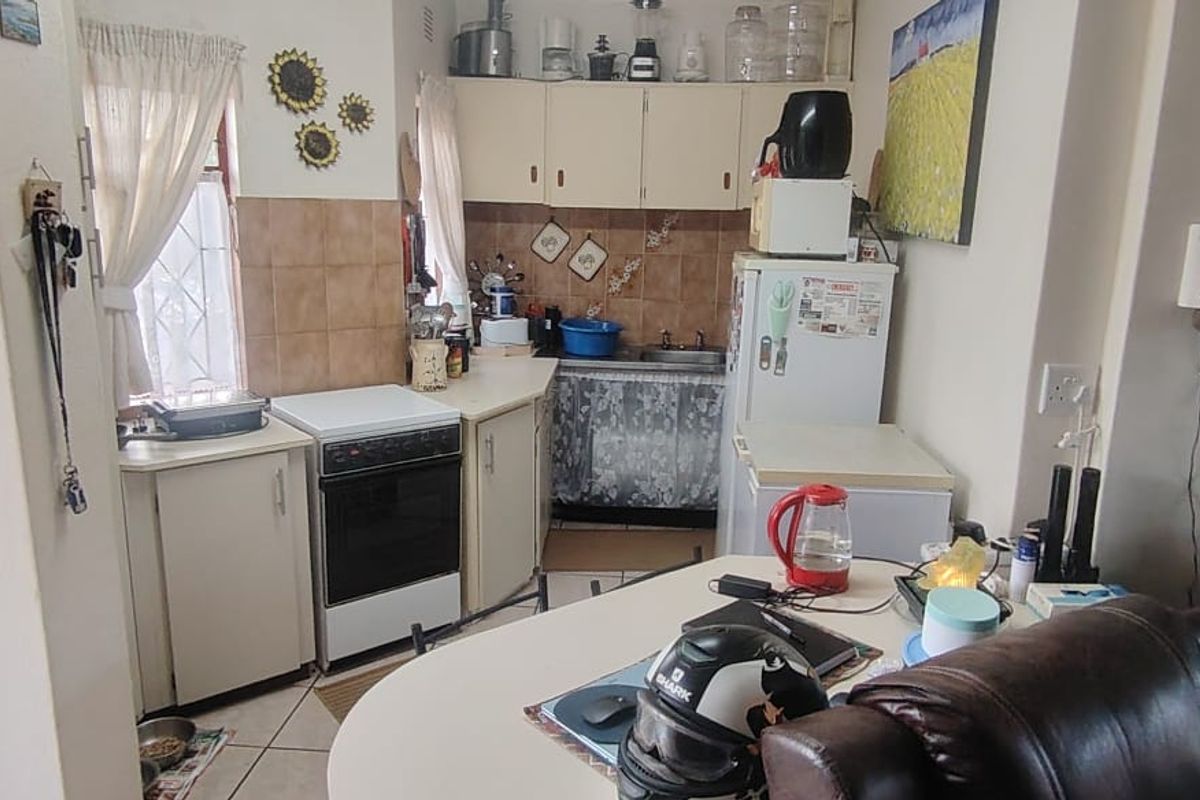 A compact, dated kitchen featuring built-in cabinetry, a freestanding stove, and tiled splashbacks, requiring modernization to improve functionality and aesthetic appeal.