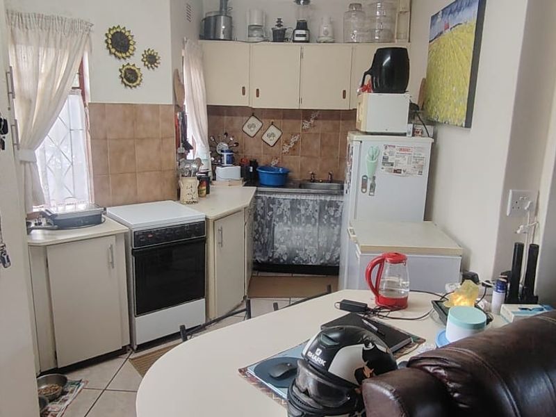 A compact, dated kitchen featuring built-in cabinetry, a freestanding stove, and tiled splashbacks, requiring modernization to improve functionality and aesthetic appeal.