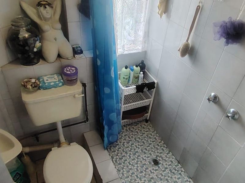 A compact bathroom featuring a toilet and a tiled shower area with dated finishes, requiring modernization to improve functionality and aesthetic appeal.