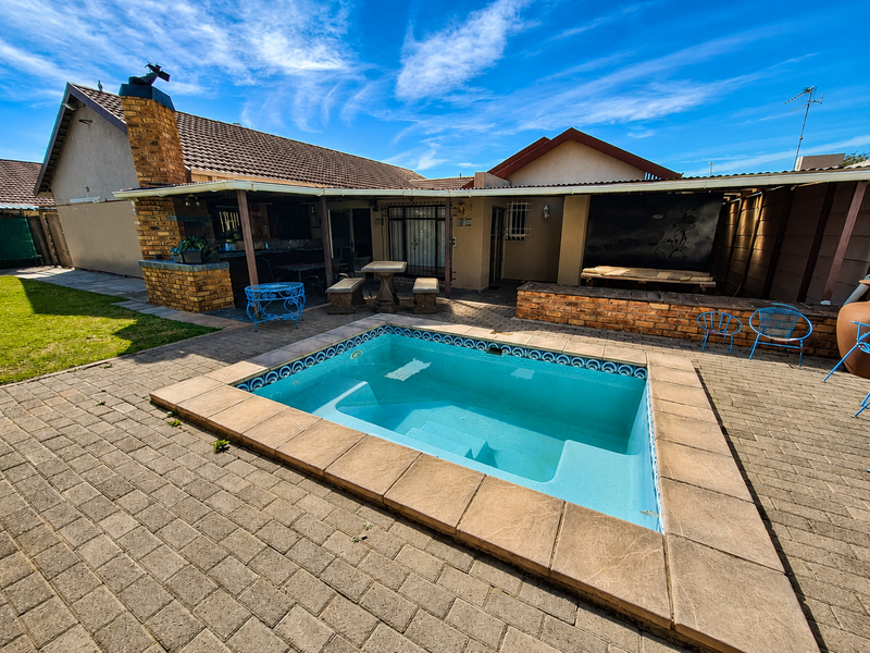 Outdoor pool area featuring a paved deck, covered patio space, and a brick chimney, ideal for outdoor entertaining.