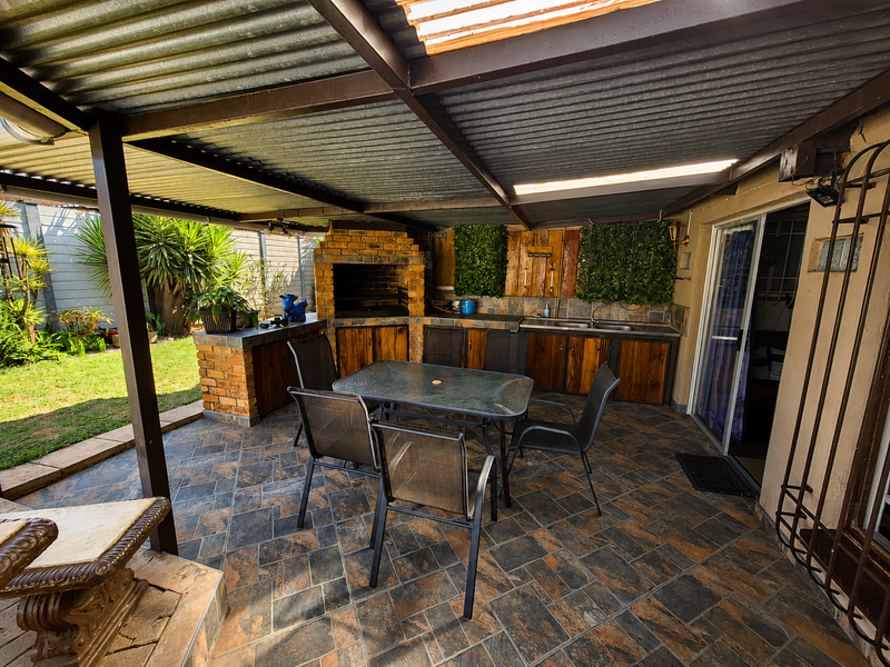 Covered outdoor patio featuring a built-in brick braai, integrated cabinetry with a sink, and durable slate tile flooring, perfect for alfresco dining.