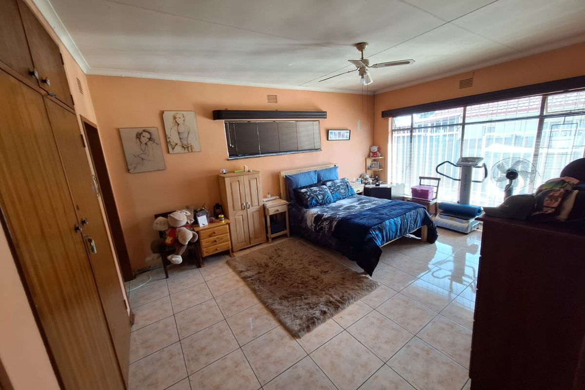 Spacious bedroom featuring tiled flooring, built-in cupboards, and a ceiling fan, offering a functional layout with ample natural light.
