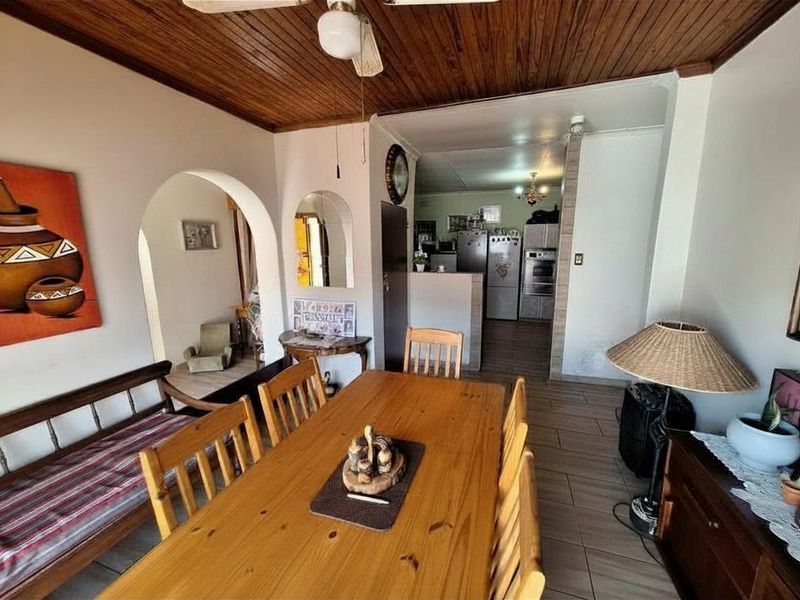 Open plan dining area featuring timber ceilings and tiled flooring, leading through an archway into a functional kitchen space.